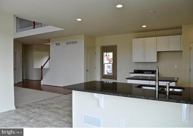 kitchen with a kitchen bar, light wood-type flooring, dark stone counters, sink, and white cabinets