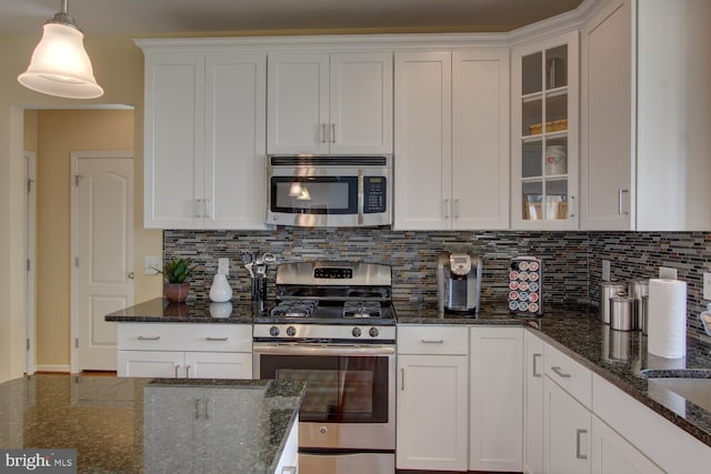 kitchen with dark stone counters, white cabinetry, hanging light fixtures, and stainless steel appliances