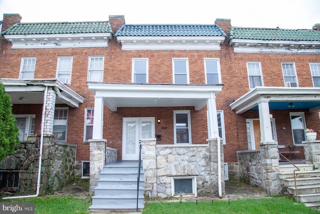 townhome / multi-family property featuring a tiled roof, a porch, and brick siding