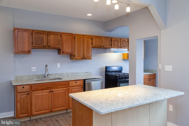 kitchen featuring black range with gas stovetop, stainless steel dishwasher, under cabinet range hood, light wood-style flooring, and brown cabinetry