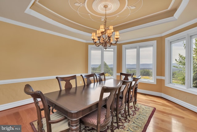 dining area featuring a notable chandelier, light wood-type flooring, and a raised ceiling