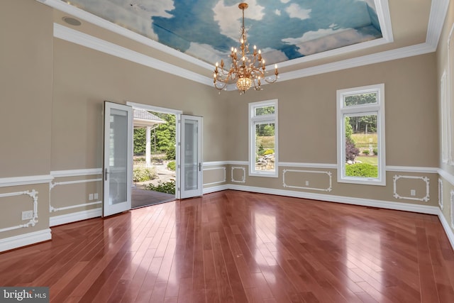 empty room with a chandelier, ornamental molding, hardwood / wood-style floors, and a tray ceiling