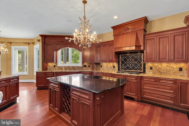 kitchen with dark stone countertops, dark hardwood / wood-style flooring, custom range hood, a chandelier, and a center island