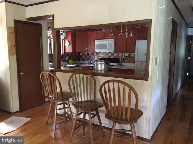 kitchen with white appliances, dark hardwood / wood-style floors, decorative backsplash, ornamental molding, and kitchen peninsula