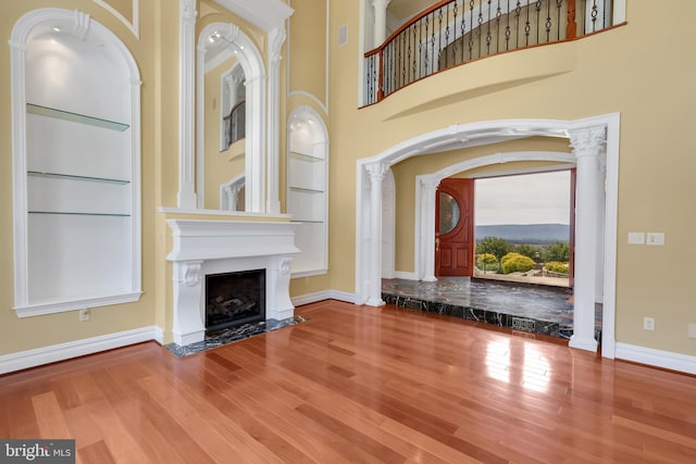 unfurnished living room with decorative columns, a fireplace, built in features, and hardwood / wood-style floors