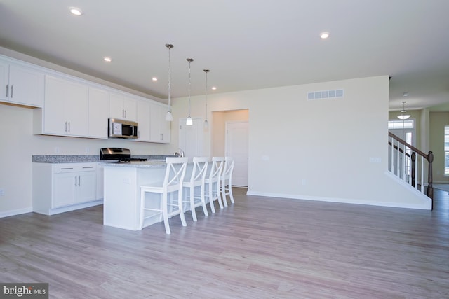 kitchen with range, a center island with sink, light hardwood / wood-style floors, and white cabinetry