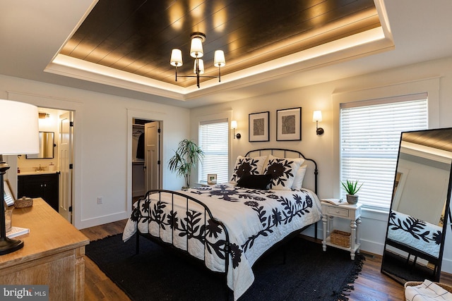 bedroom featuring a walk in closet, a raised ceiling, ensuite bath, and dark wood-type flooring