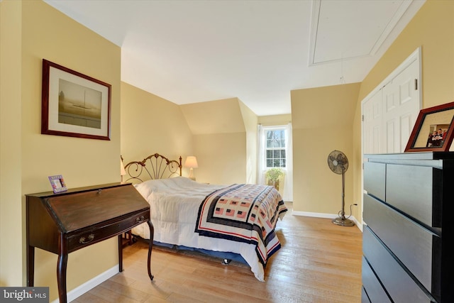 bedroom with attic access, light wood finished floors, and baseboards
