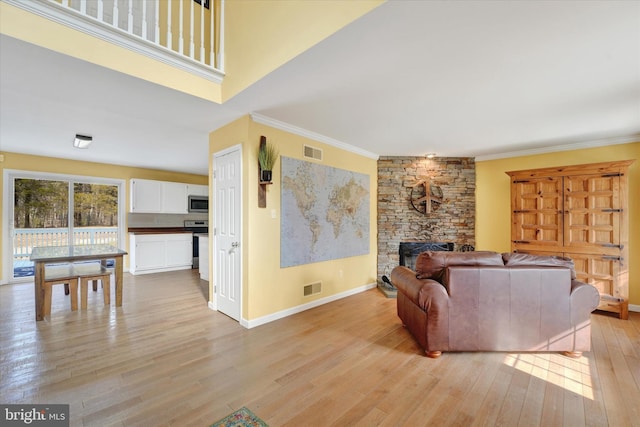 living area with visible vents, baseboards, crown molding, and light wood-style floors