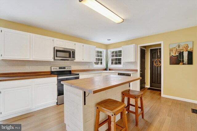 kitchen featuring wood counters, stainless steel appliances, light wood-style floors, white cabinets, and a kitchen breakfast bar