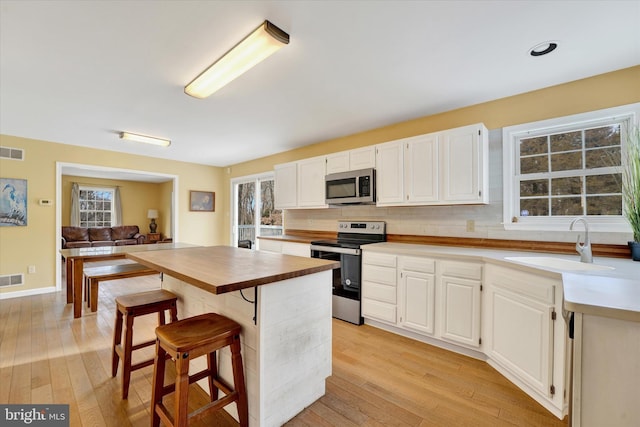 kitchen featuring a sink, light wood-style flooring, white cabinets, appliances with stainless steel finishes, and butcher block counters