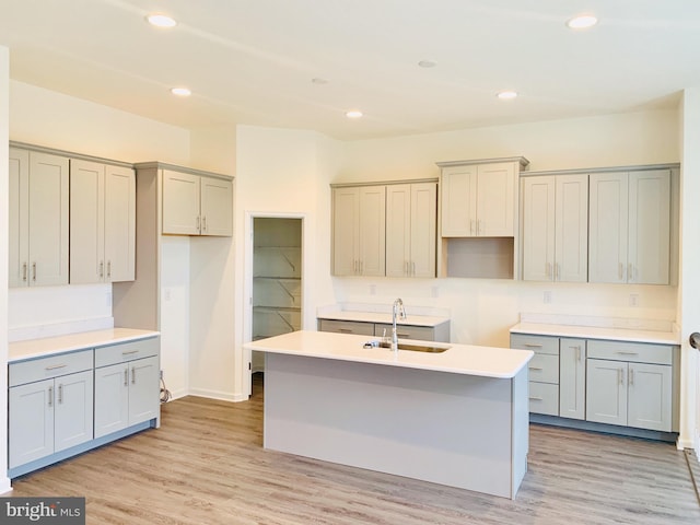 kitchen featuring gray cabinetry, light hardwood / wood-style flooring, an island with sink, and sink