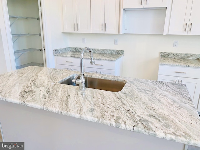 kitchen with white cabinets, light stone countertops, and sink