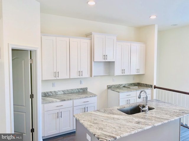 kitchen with light stone countertops, sink, dark hardwood / wood-style flooring, an island with sink, and white cabinets