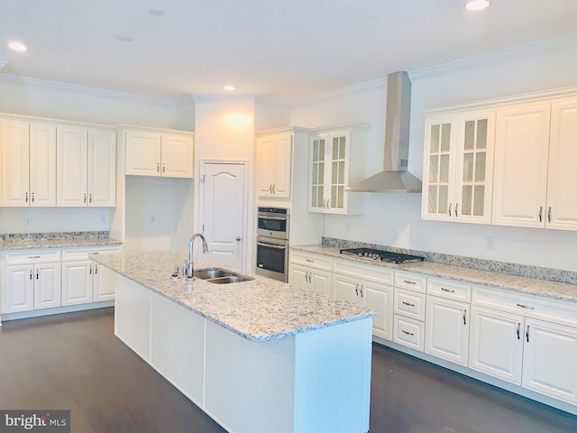 kitchen featuring white cabinetry, sink, stainless steel appliances, wall chimney range hood, and a kitchen island with sink