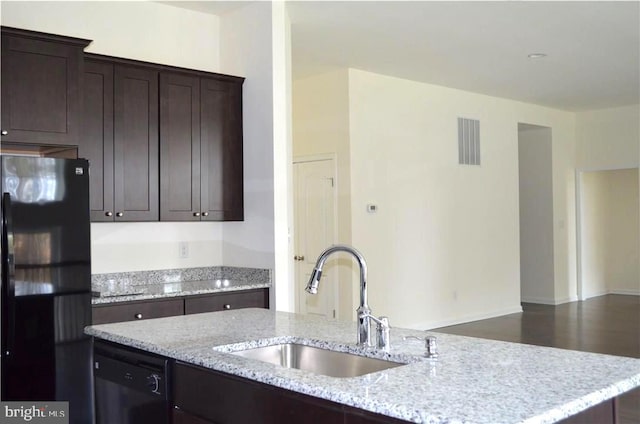 kitchen featuring dishwasher, black refrigerator, light stone countertops, and sink