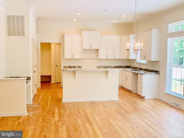 kitchen featuring white cabinets, light wood-type flooring, hanging light fixtures, and a healthy amount of sunlight