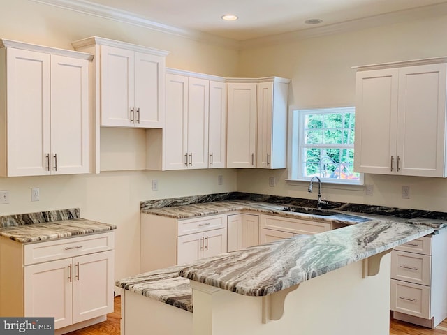 kitchen featuring white cabinets, crown molding, light stone countertops, a kitchen breakfast bar, and sink