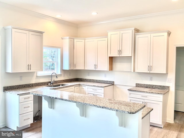 kitchen featuring light stone countertops, a breakfast bar area, a kitchen island, sink, and light hardwood / wood-style flooring