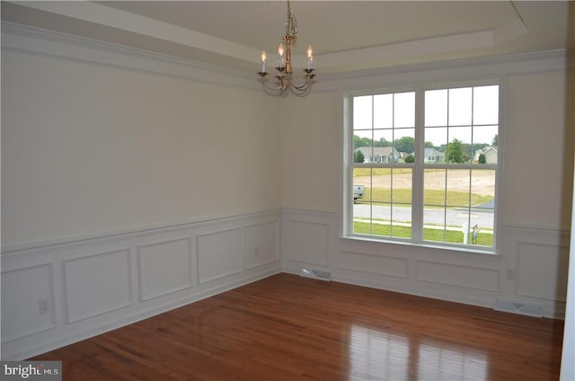 empty room with wood-type flooring, a tray ceiling, and a chandelier