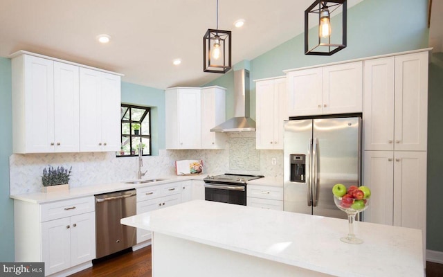 kitchen with wall chimney range hood, sink, appliances with stainless steel finishes, decorative light fixtures, and white cabinetry