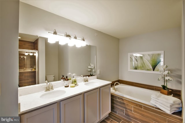 bathroom featuring toilet, double vanity, and a relaxing tiled bath