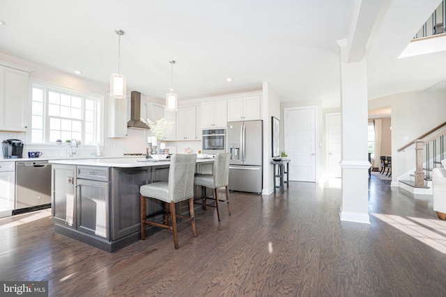 kitchen with white cabinets, a center island, stainless steel appliances, and wall chimney range hood