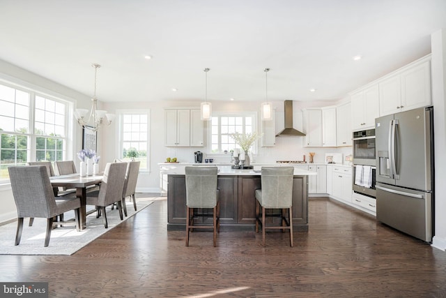 kitchen featuring appliances with stainless steel finishes, wall chimney range hood, decorative light fixtures, a center island, and white cabinetry