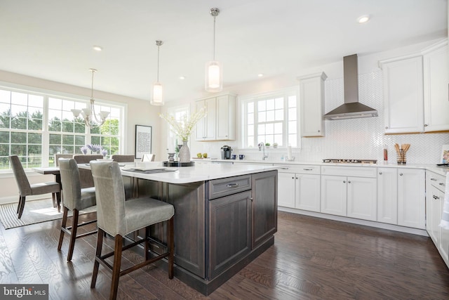 kitchen featuring white cabinets, pendant lighting, a center island, and wall chimney range hood