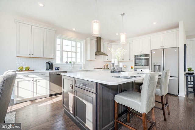 kitchen featuring wall chimney exhaust hood, a kitchen island, white cabinetry, and appliances with stainless steel finishes