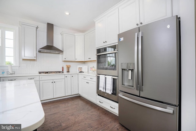 kitchen featuring white cabinetry, stainless steel appliances, wall chimney range hood, light stone counters, and dark hardwood / wood-style floors