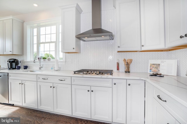 kitchen with sink, wall chimney range hood, light stone counters, backsplash, and white cabinets