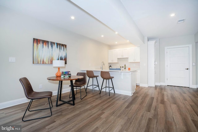 kitchen featuring dark wood-type flooring, white cabinets, sink, a kitchen bar, and kitchen peninsula