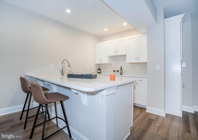 kitchen with white cabinetry, sink, dark hardwood / wood-style floors, kitchen peninsula, and a breakfast bar area