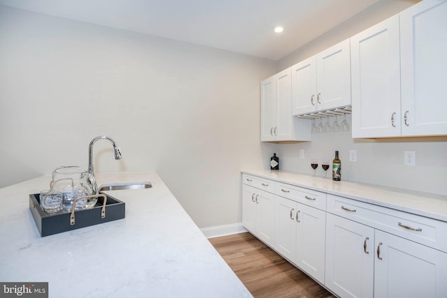 kitchen with light wood-type flooring, white cabinetry, and sink