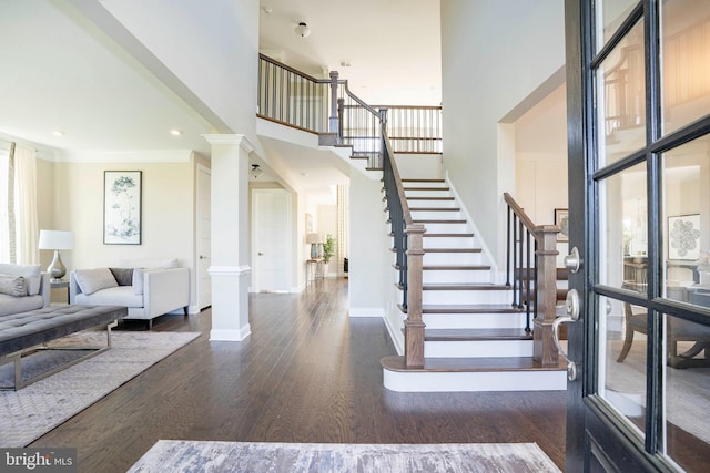 foyer with ornamental molding, dark wood-type flooring, a high ceiling, and decorative columns