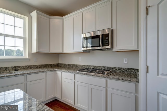 kitchen with dark hardwood / wood-style flooring, white cabinets, light stone countertops, and stainless steel appliances