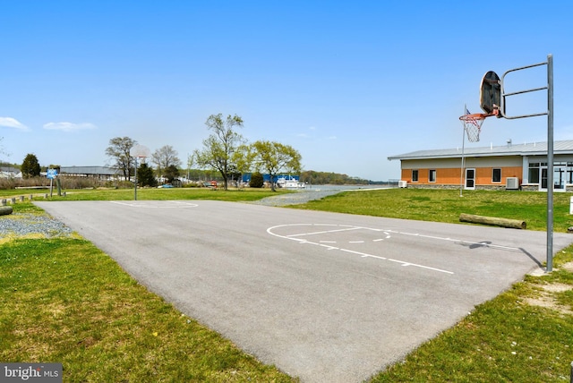 view of sport court with a lawn and a water view