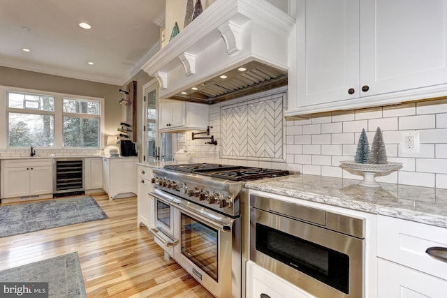 kitchen with beverage cooler, stainless steel appliances, light hardwood / wood-style flooring, custom range hood, and ornamental molding