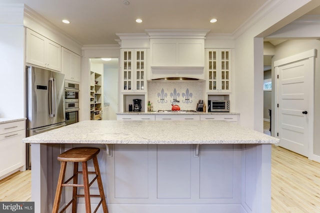 kitchen with light stone countertops, a large island, white cabinetry, stainless steel appliances, and a breakfast bar area