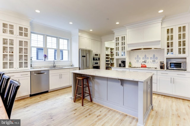 kitchen featuring white cabinets, stainless steel appliances, a kitchen island, and light stone counters