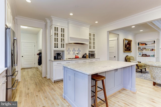 kitchen with appliances with stainless steel finishes, light stone counters, light hardwood / wood-style flooring, white cabinets, and a kitchen island