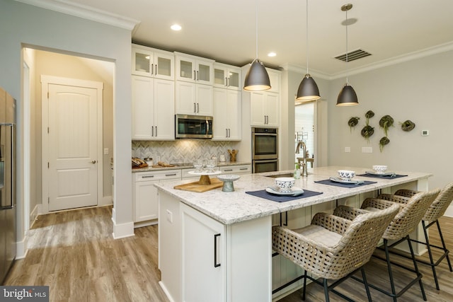 kitchen featuring a kitchen island with sink, a kitchen bar, white cabinetry, and stainless steel appliances