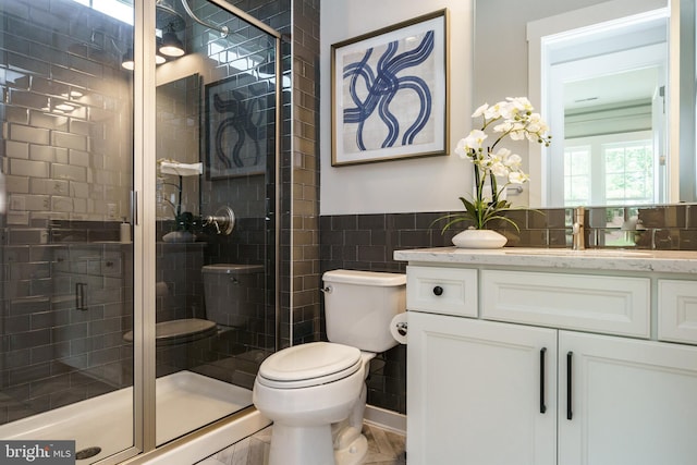 bathroom with vanity, tile walls, tile flooring, toilet, and a shower with shower door