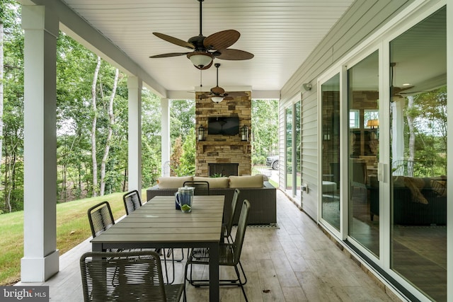 sunroom / solarium featuring plenty of natural light, an outdoor stone fireplace, and ceiling fan