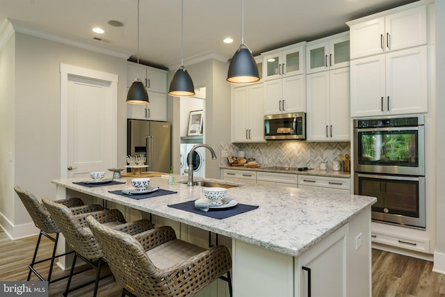 kitchen with a kitchen island with sink, stainless steel appliances, white cabinets, and decorative light fixtures