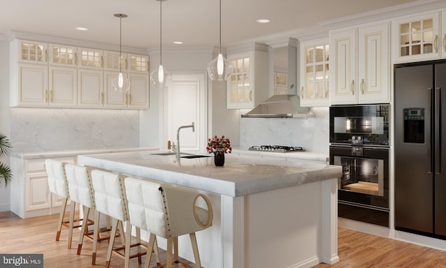 kitchen featuring wall chimney exhaust hood, light stone countertops, a kitchen island with sink, and appliances with stainless steel finishes