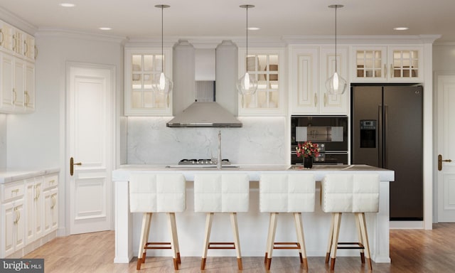 kitchen featuring a kitchen bar, wall chimney range hood, stainless steel fridge with ice dispenser, hanging light fixtures, and an island with sink