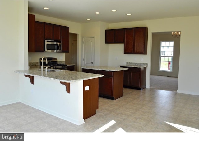 kitchen with light stone counters, a notable chandelier, light tile floors, range with gas cooktop, and sink