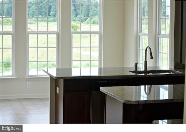 kitchen featuring dark brown cabinetry, sink, light tile floors, and stone countertops